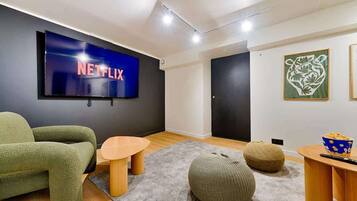 A modern living room with a large flat-screen TV displaying 'NETFLIX', a green sofa, a wooden coffee table, and a popcorn bowl.
