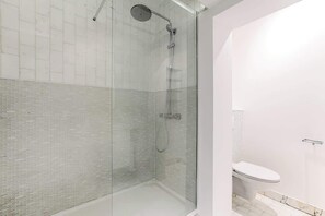 Un baño moderno con ducha de vidrio, inodoro blanco y suelo de baldosas.