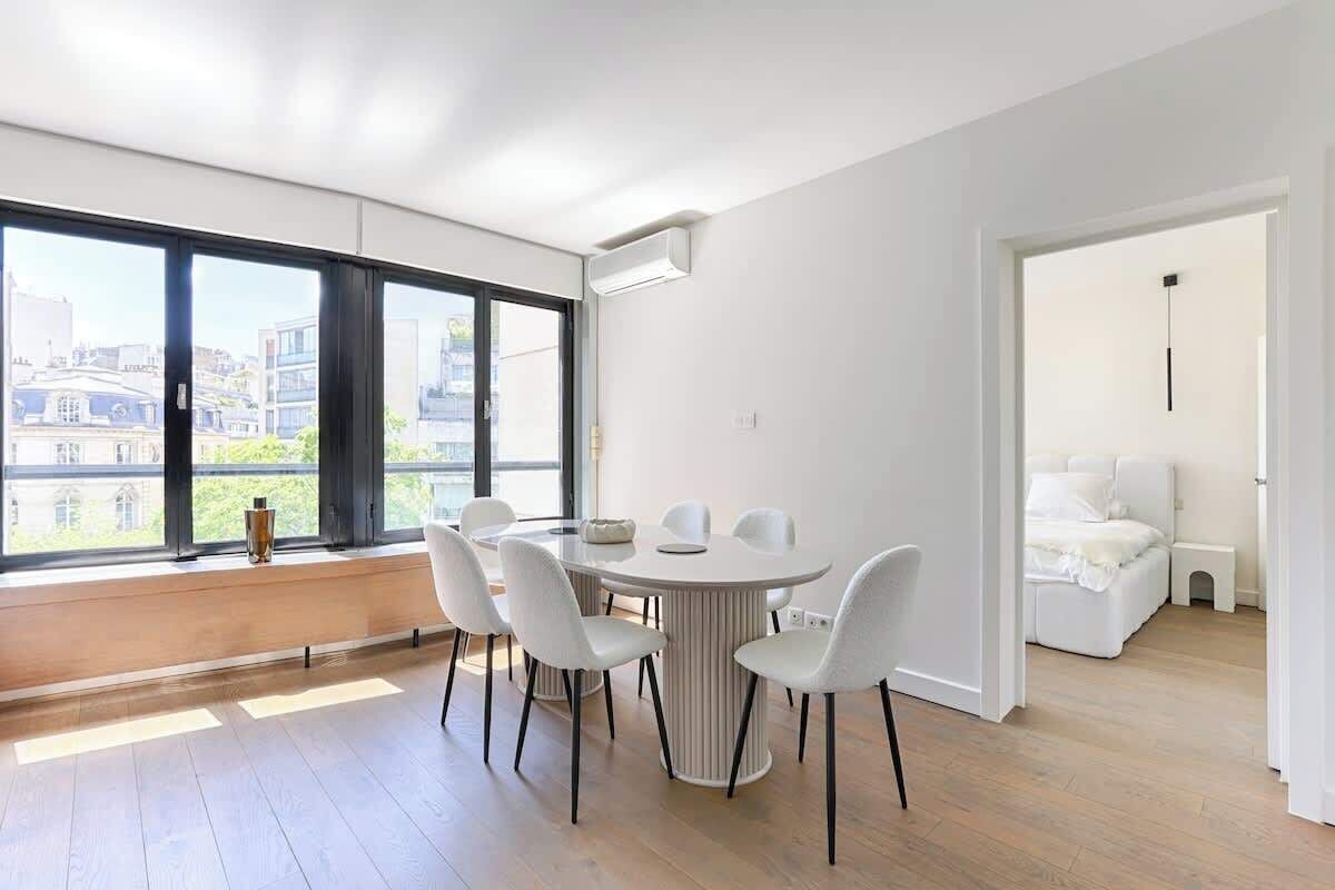 Un apartamento moderno con comedor, ventanas amplias y vista a edificios.