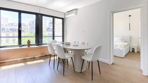 A modern apartment with a dining area, large windows, and a view of buildings.