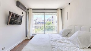 A bedroom with a large bed, a sliding glass door to a balcony, and a mounted air conditioning unit.