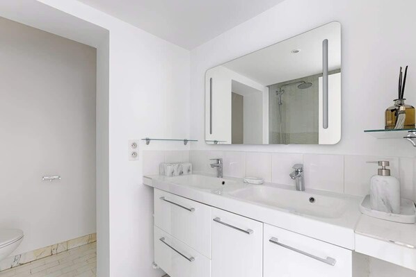 A modern bathroom with a white vanity, a large mirror, and a glass shelf with toiletries.