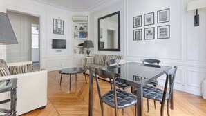 A modern living room with a dining area, white walls, and a large mirror. - Appartement de Luxe sur les Invalides (Paris)