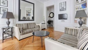 A living room with two striped sofas, a round coffee table, and a large mirror. - Appartement de Luxe sur les Invalides (Paris)