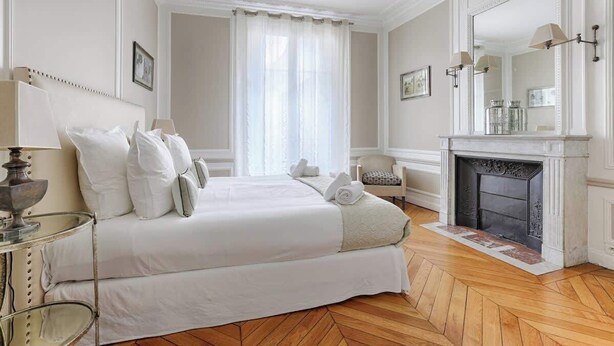 A hotel room with a large bed, a fireplace, and a mirror. - Appartement de Luxe sur les Invalides (Paris)