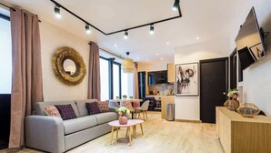Un salon moderne avec un canapé gris, un miroir rond et un coin repas comprenant une petite table et des chaises.