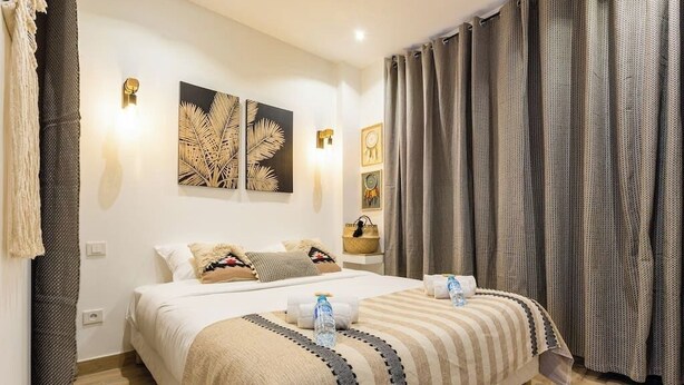 Une chambre d’hôtel avec un grand lit, deux lampes fixées au mur et une fenêtre avec des rideaux.