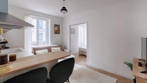 Un apartamento moderno con cocina, comedor y sala de estar. Cuenta con un ventanal grande, un televisor de pantalla plana e iluminación en el techo.