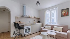 Una cocina moderna con armarios blancos, una silla negra y un sofá color beige con una mesita de centro blanca.
