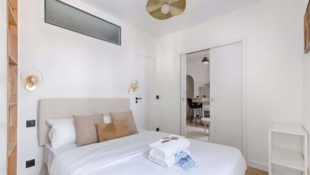 Una habitación de hotel moderna con una cama grande, una mesita de noche, un armario y un baño visible a través de una puerta abierta.