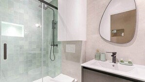 Un baño moderno con ducha de vidrio, inodoro blanco, lavabo con espejo y artículos de aseo en la encimera.