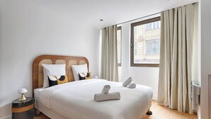 Et hotelværelse med en stor seng, et natbord med en lampe og et vindue med gardiner.