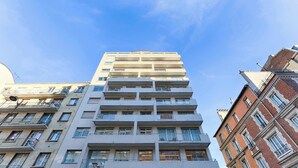Un immeuble à plusieurs étages, doté de balcons, de grandes fenêtres et surplombant un ciel d’un bleu éclatant.
