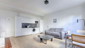 Un salon moderne avec un canapé gris, une table basse en verre et un coin repas comprenant une chaise en bois.