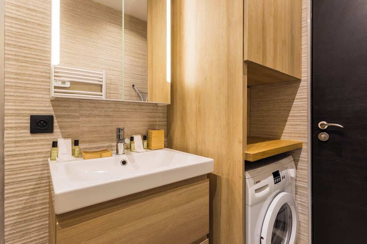 Un baño moderno con tocador de madera, lavamanos, espejo y lavadora.