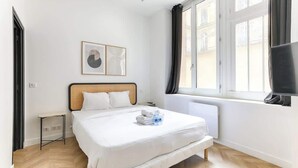 Une chambre d’hôtel moderne avec un grand lit, une petite table de chevet, un téléviseur à écran plat et une fenêtre avec des rideaux.