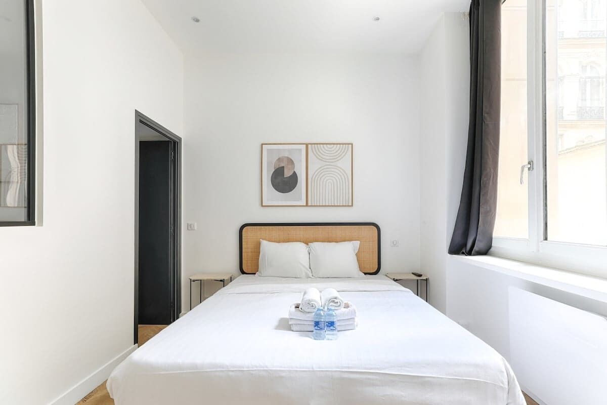 A hotel room with a bed, a nightstand, a framed artwork above the bed, and a window with curtains.