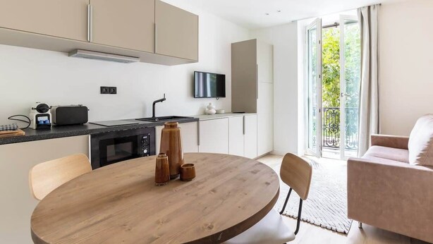 Eine moderne Küche mit einem runden Holztisch, einem über der Arbeitsfläche montierten Fernseher und einer Glastür zum Balkon.