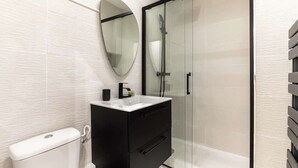 Ein modernes Badezimmer mit Toilette, einem schwarzen Waschtisch mit Spiegel und einer Duschkabine.