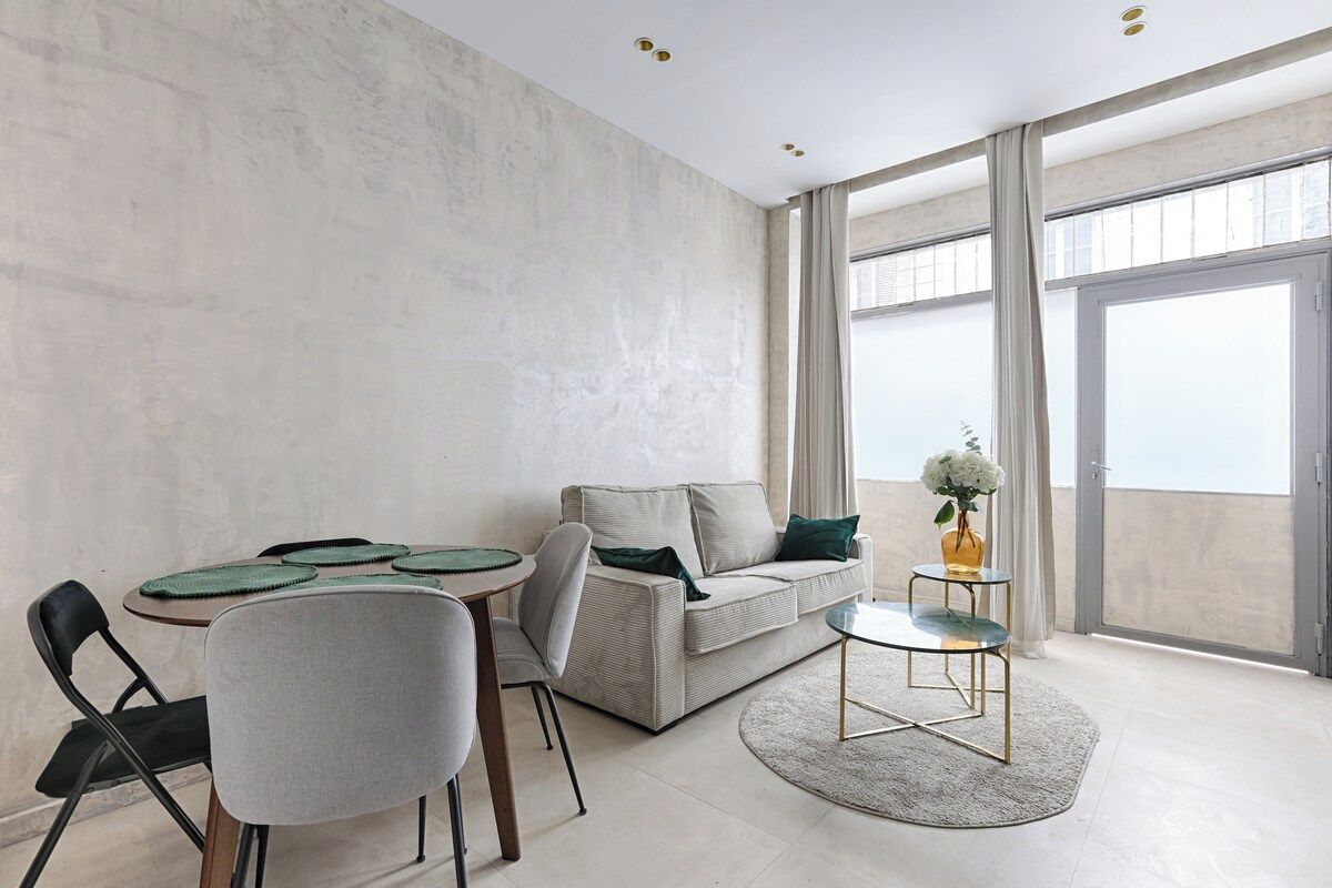 Un salon moderne comprenant un canapé, des fauteuils, une table basse et une table à manger avec des sets de table.