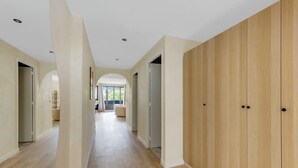 Un corridoio moderno con pavimento in legno e pareti chiare, che conduce a una zona relax con vista sul verde esterno.
