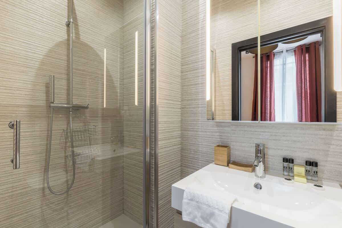 A modern bathroom with a glass-enclosed shower, a white sink with a mirror above it, and a wooden box on the counter.