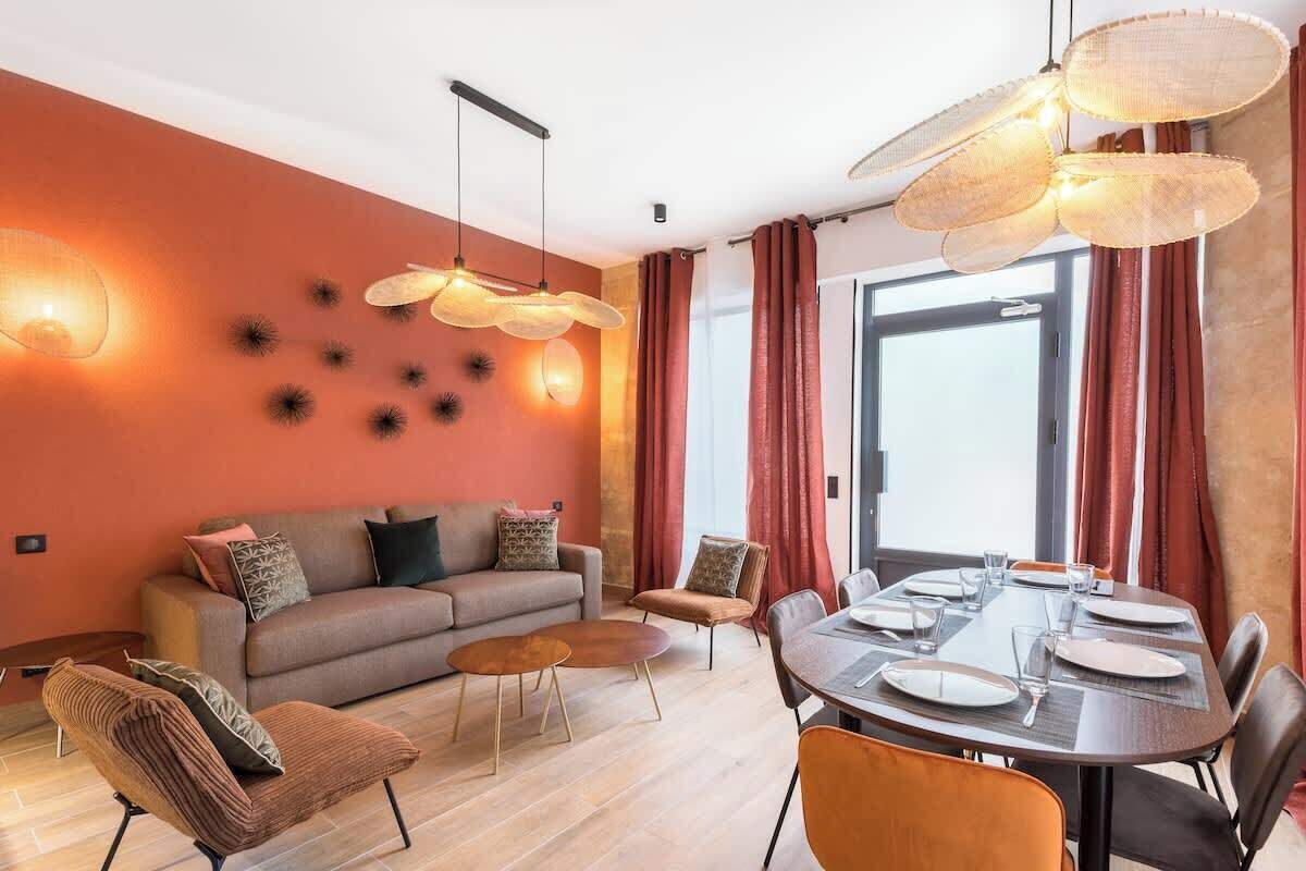 Una sala de estar moderna con un sofá, una mesa de centro, una mesa de comedor preparada para cuatro comensales y un ventanal con cortinas.