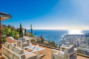 Une terrasse avec des sièges extérieurs, une rambarde en verre et une vue sur la ville.