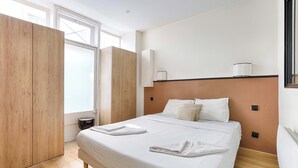 A bedroom with a large bed, wooden wardrobe, and a window with blinds. - Appartement Cosy au cœur de Batignolles (Paris)
