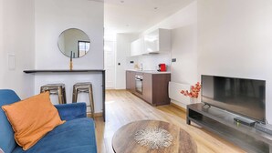 A modern living room with a blue sofa, a round coffee table, and a flat-screen TV. - Appartement Cosy au cœur de Batignolles (Paris)