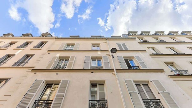 A multi-story building with a flat facade, multiple windows with shutters, and a clear sky with clouds. - Appartement Cosy au cœur de Batignolles (Paris)