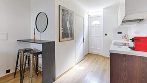 A modern kitchen with a white countertop, a red appliance, and a framed cityscape artwork. - Appartement Cosy au cœur de Batignolles (Paris)