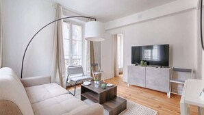 A modern living room with a sofa, a coffee table, a TV, and a cabinet. - Laugier Ternes : Appartement Cosy en Bail Mobilité (Paris)