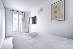 Een moderne hotelkamer met een groot bed, een flatscreen televisie aan de muur en een raam met gordijnen.