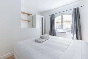 A bedroom with a bed, a window with curtains, a wardrobe, and a mirror.