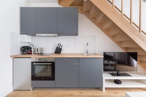 A modern kitchen with grey cabinets, a wooden countertop, a built-in oven, a sink, and a television on a white shelf.