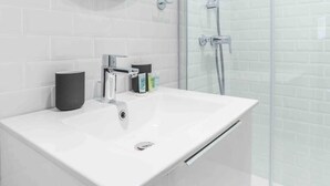 A modern bathroom with a white sink, a round mirror, and a glass shower enclosure. - Marivaux/Opéra : Charming & Cosy Duplex 4P-1BR (Paris)