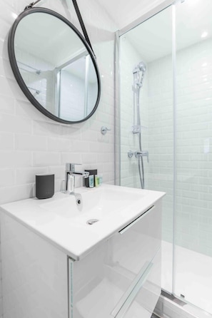 A modern bathroom with a white sink, a round mirror, and a glass shower enclosure.