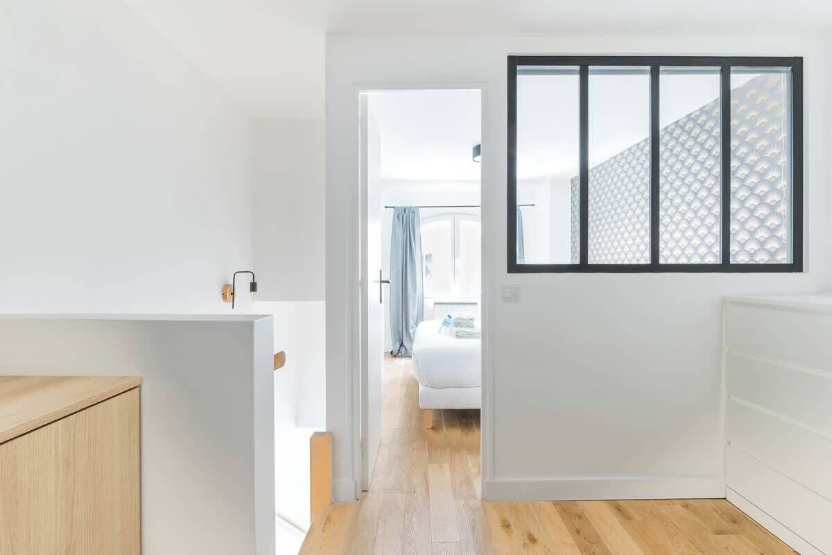 Un pasillo con suelo de madera, pared blanca y una ventana con diseño geométrico.