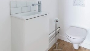 A modern bathroom with a white vanity, a round mirror, a toilet, and a bidet. - Marivaux/Opéra : Charming & Cosy Duplex 4P-1BR (Paris)