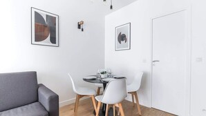 A modern dining area with a round table, white chairs, and a grey sofa. - Marivaux/Opéra : Charming & Cosy Duplex 4P-1BR (Paris)