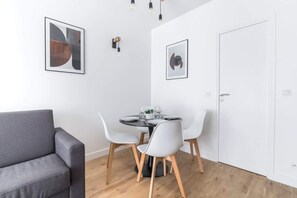 Een moderne eethoek met een ronde tafel, witte stoelen en een grijze bank.