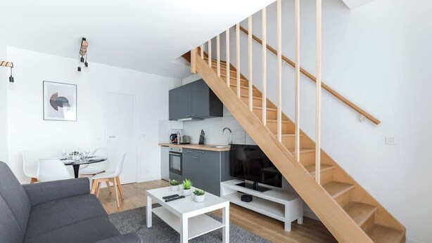 A modern living space with a grey sofa, a white coffee table, a kitchen with grey cabinets, and a wooden staircase. - Marivaux/Opéra : Charming & Cosy Duplex 4P-1BR (Paris)