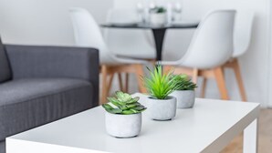 A modern living room with a white table, two potted plants, a grey sofa, and a dining area in the background. - Marivaux/Opéra : Charming & Cosy Duplex 4P-1BR (Paris)