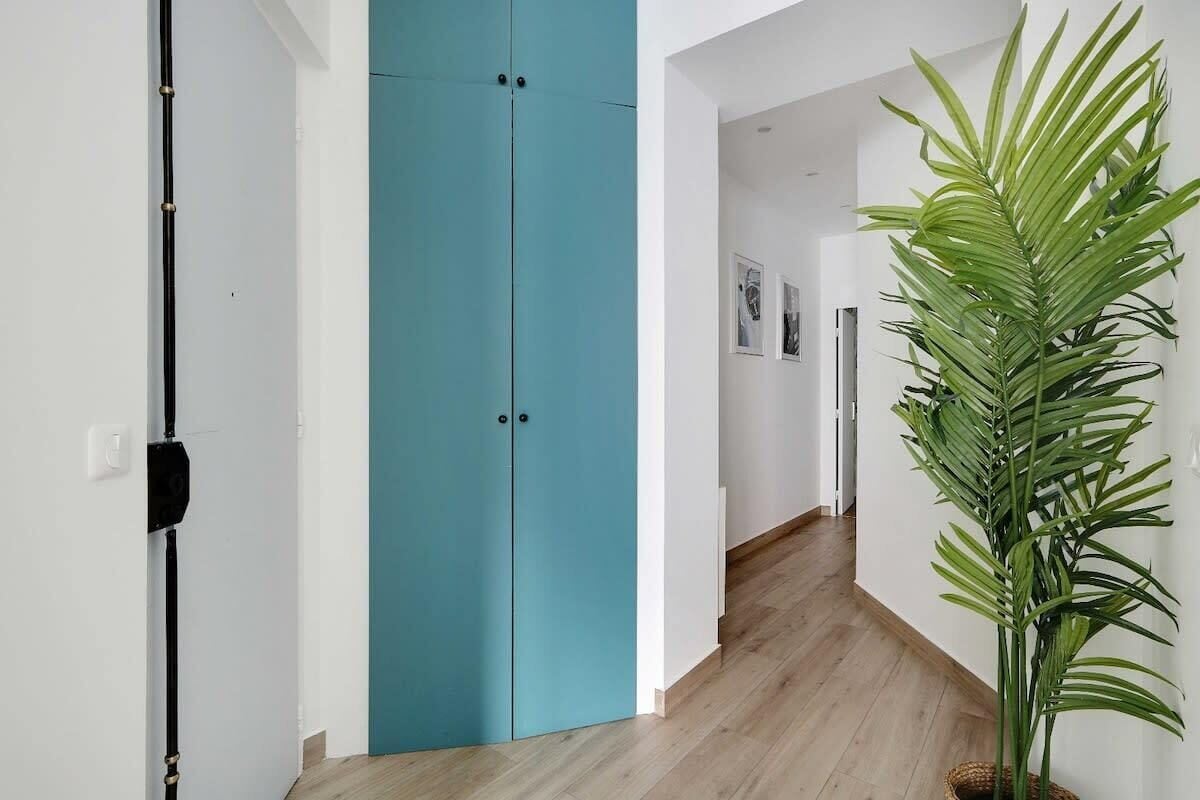 Un couloir avec une porte de couleur turquoise, une plante et un plancher en bois.