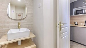 Un baño moderno con un lavabo rectangular, un espejo y una puerta que da a una zona de cocina.