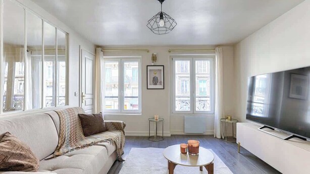Una sala de estar con un sofá, una mesa de centro, un televisor y ventanas grandes.