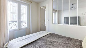 Un dormitorio con cama, un ventanal grande, televisión y espejo.