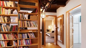 Ein Flur mit Holzböchenregalen, gefüllt mit Büchern, einer Lampe und Blick in einen Raum mit Bett und Badezimmer.