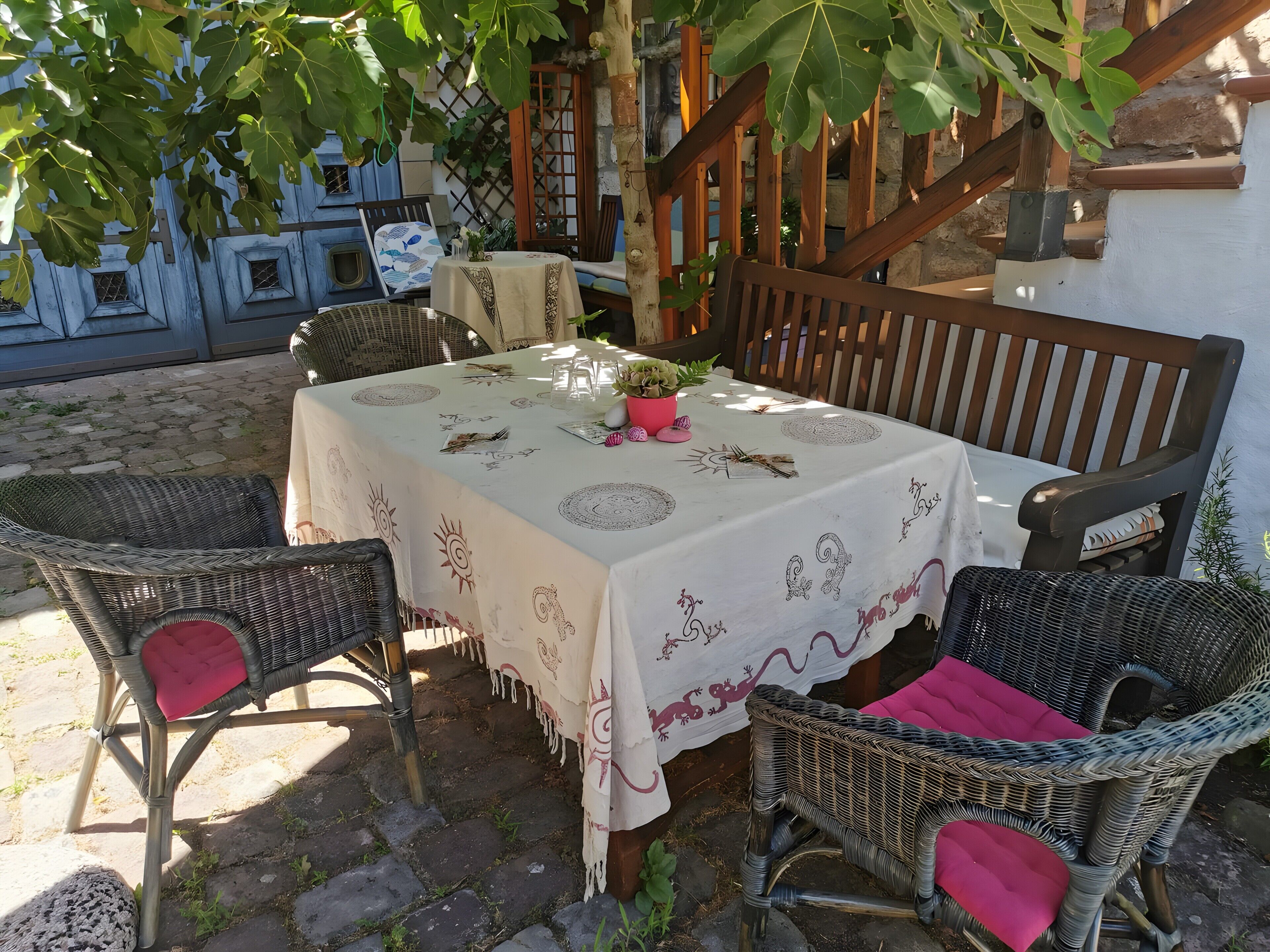 Een overdekt terras met rieten stoelen, een tafel met wit tafelkleed en een trap op de achtergrond.